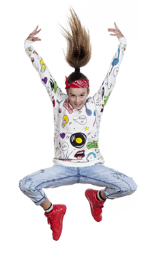 10-letnia tancerka w dynamicznym wyskoku z rękami uniesionymi nad głową, nogami szeroko ustawionymi i zgiętymi w kolanach, uśmiechnięta, w stylu hip-hop z kolorową bluzą, jasnymi dżinsami, czerwonymi sportowymi butami i czerwoną opaską na głowie